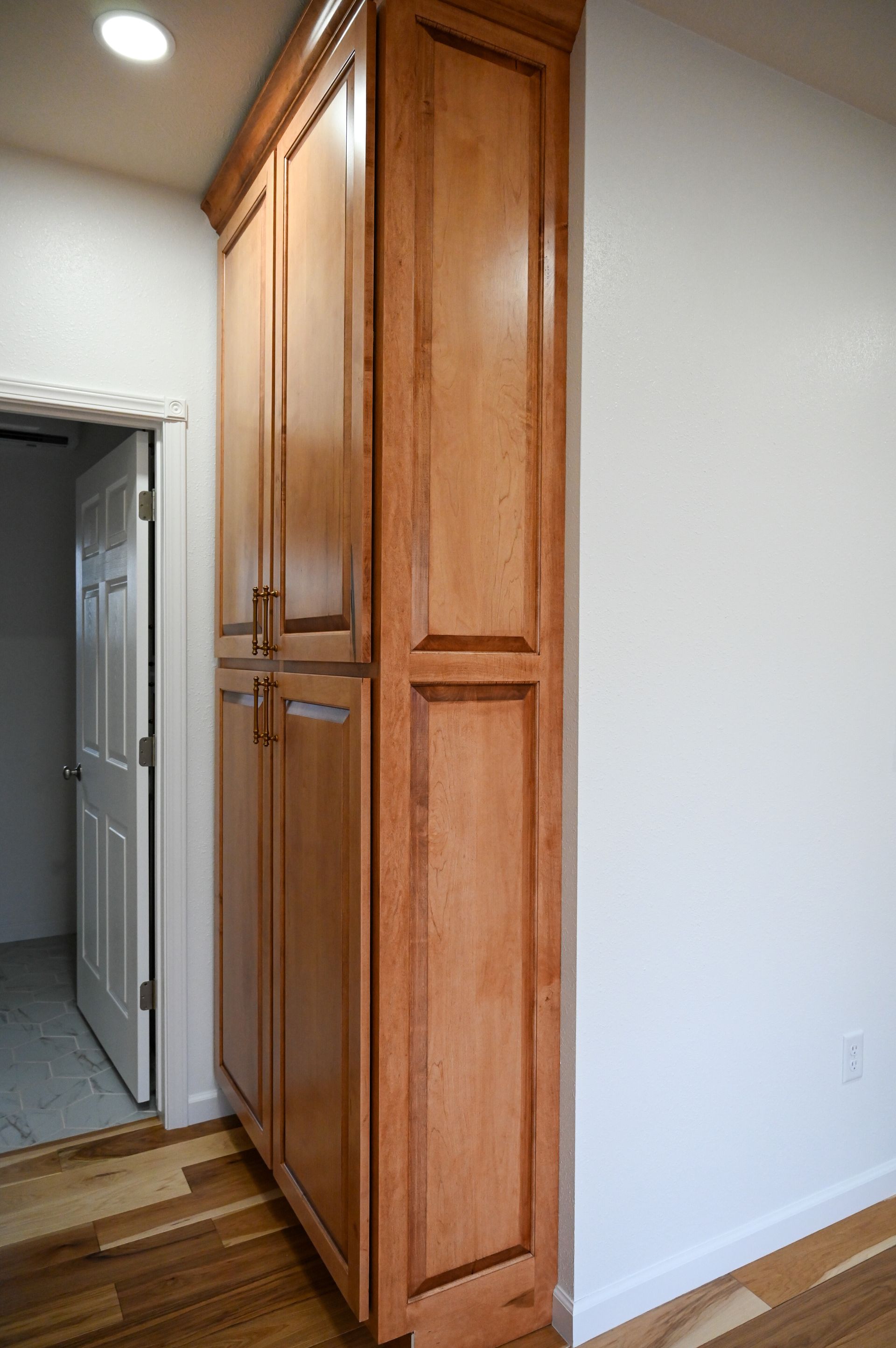 Tall wooden cabinet in a hallway next to an open doorway and white wall.
