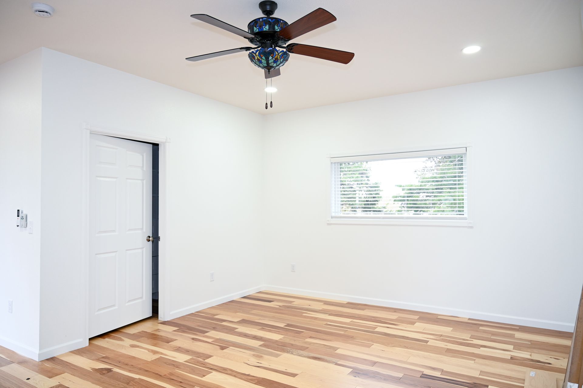 Empty white room with ceiling fan, window, closet door, and unfinished wood floor