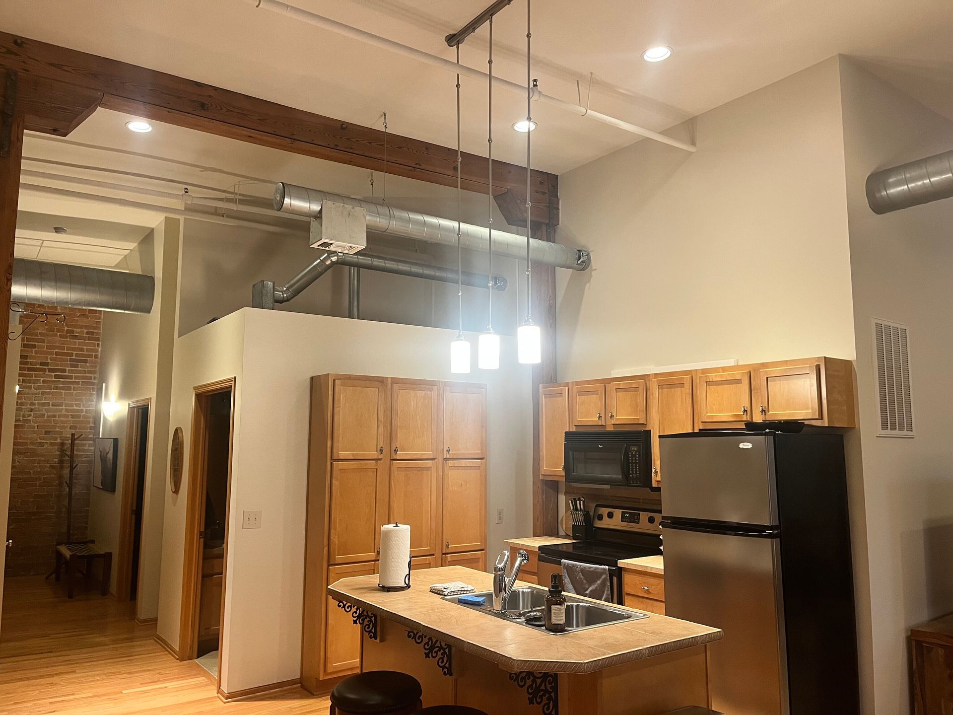 Open kitchen with wooden cabinets, island, stainless fridge, and vaulted ceiling lights