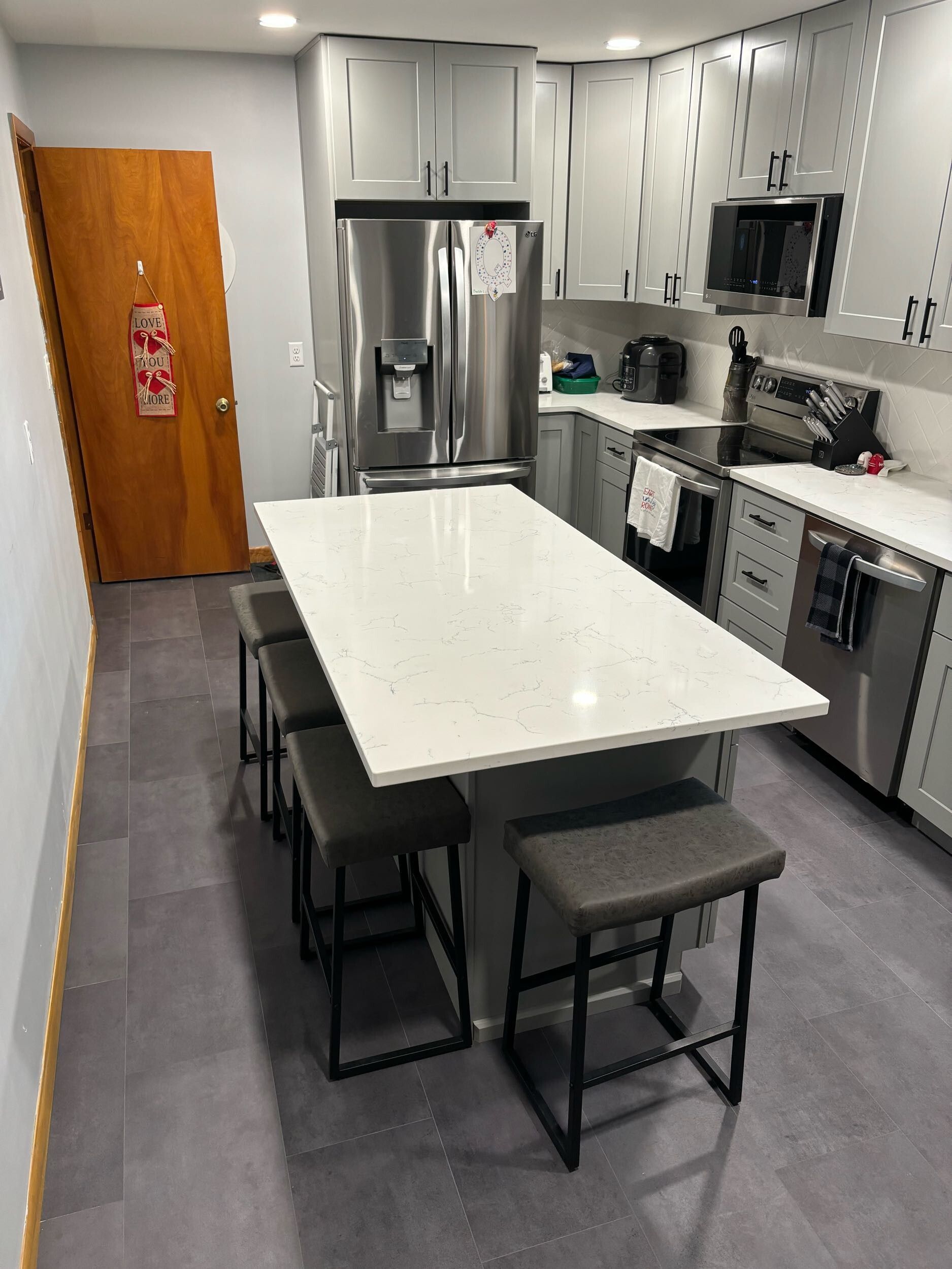 Modern kitchen with white island, stools, stainless steel appliances, and gray cabinets