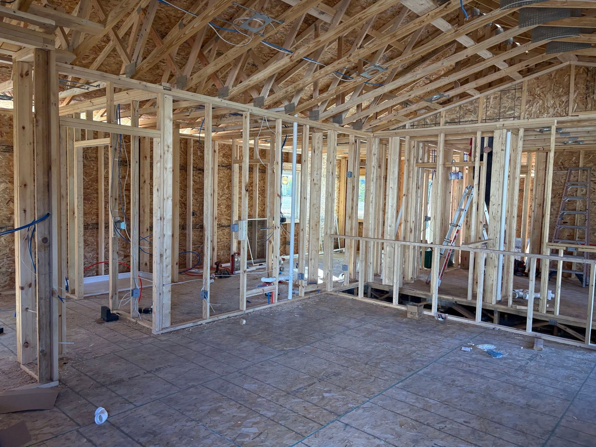 Unfinished house interior with exposed wooden framing and plywood subfloor.