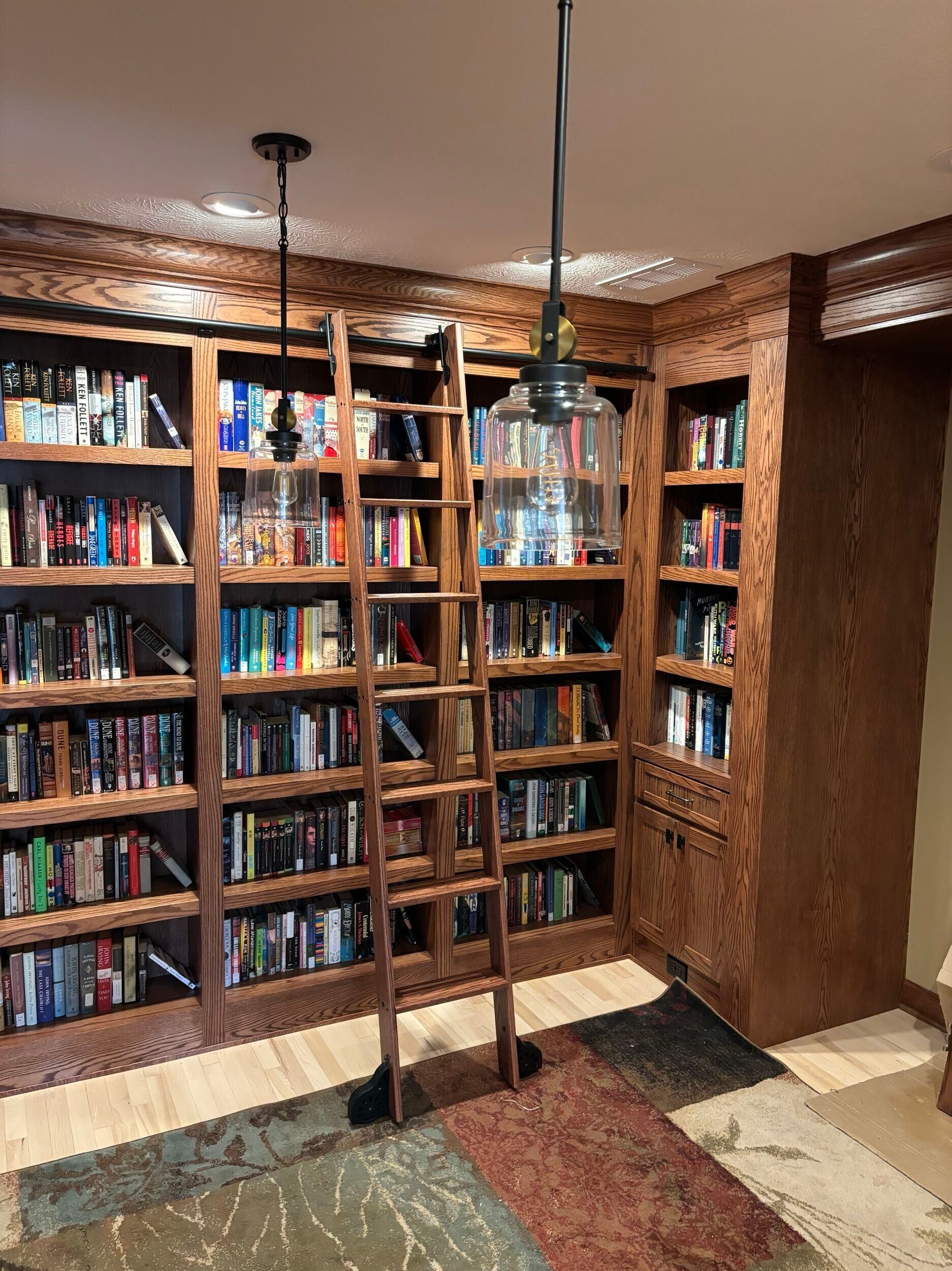 Built-in wooden bookshelf filled with books in a cozy corner, with hanging pendant lights and a small rug.