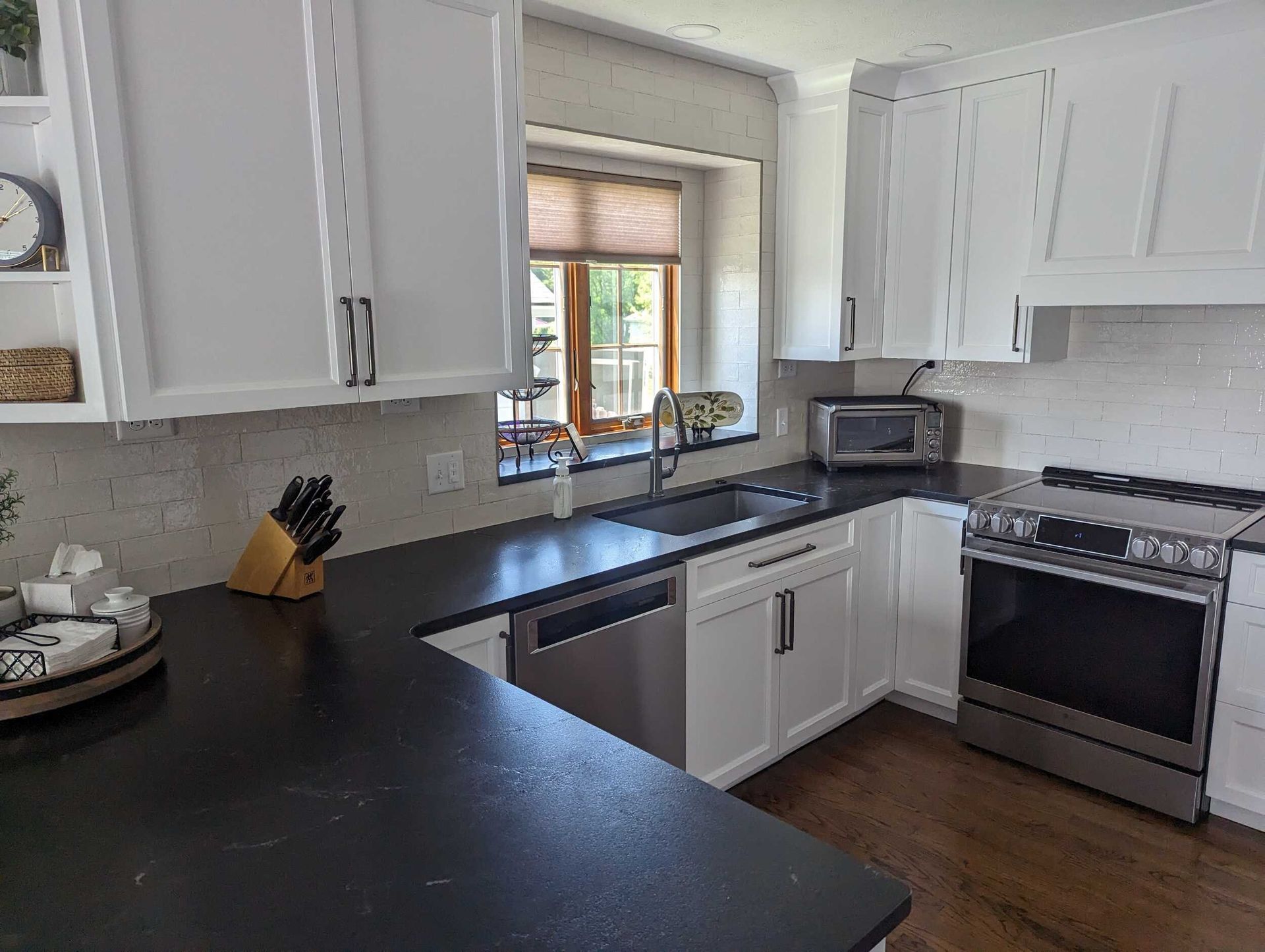 Modern white kitchen with black countertops, stainless appliances, and a window over the sink