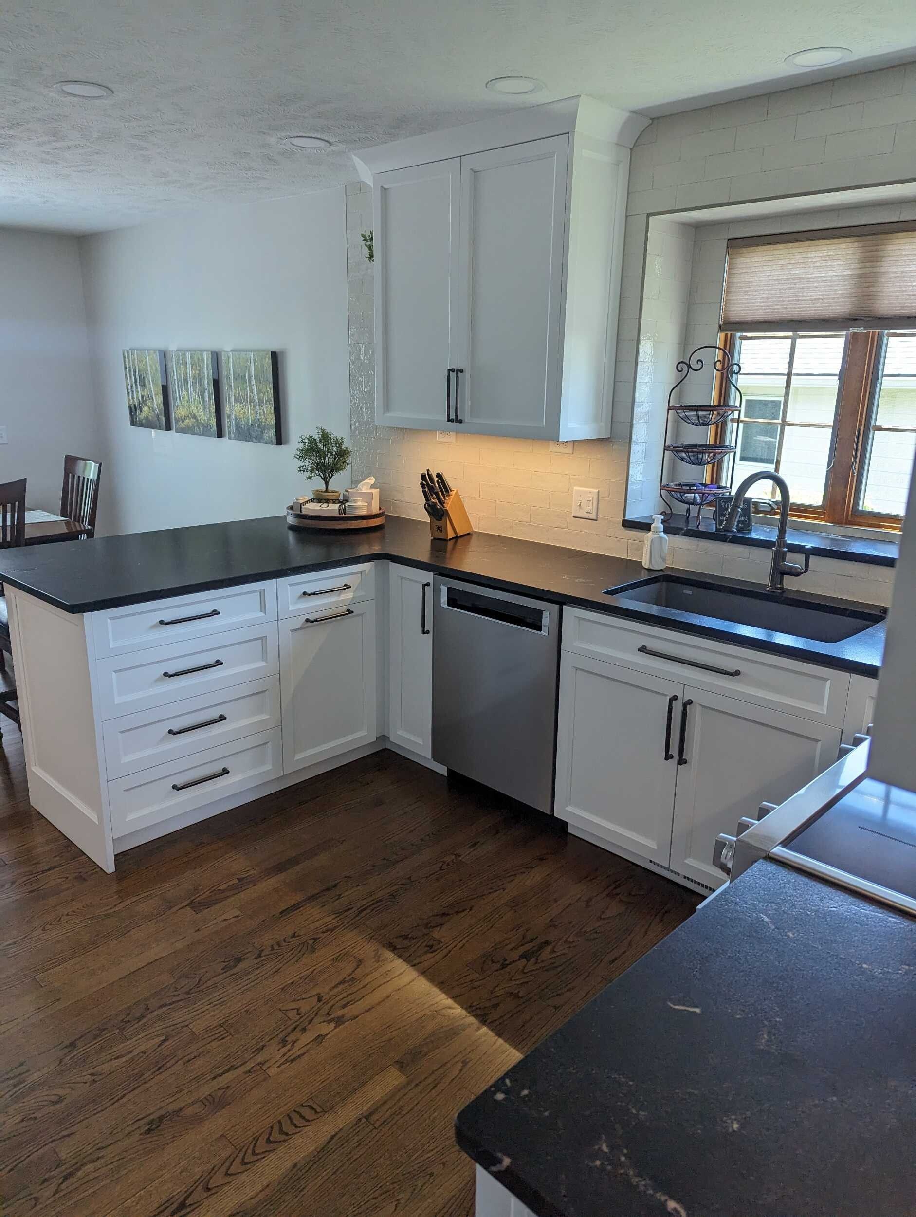Bright kitchen with white cabinets, dark countertops, hardwood floor, and sunlit window over the sink.