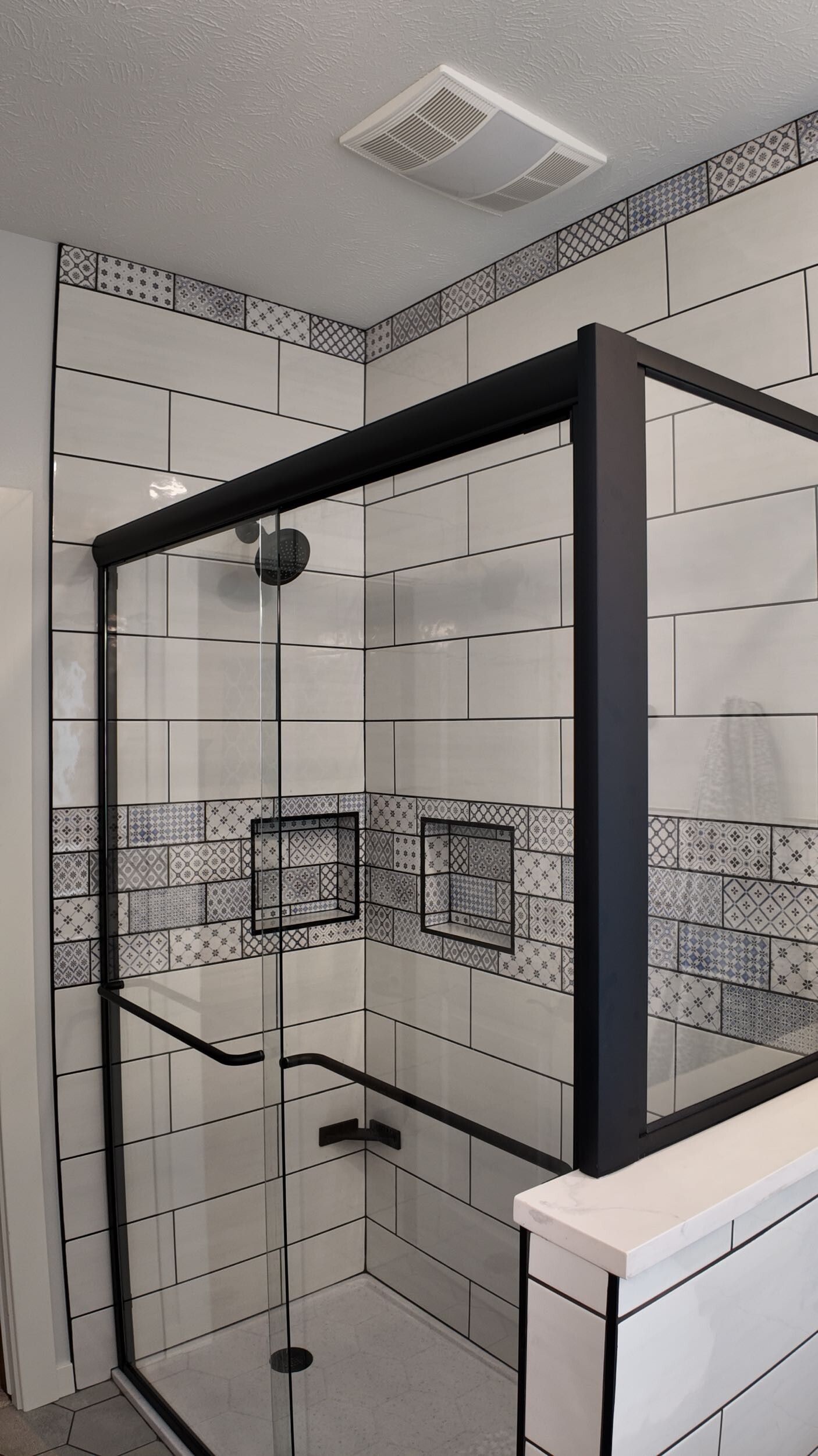 Glass shower enclosure in a white tiled bathroom with black trim.