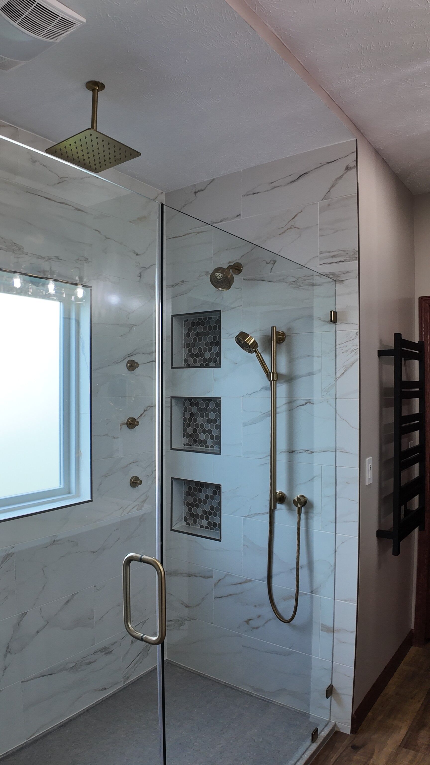 Modern bathroom shower with glass enclosure, marble-look walls, rain showerhead, and handheld sprayer