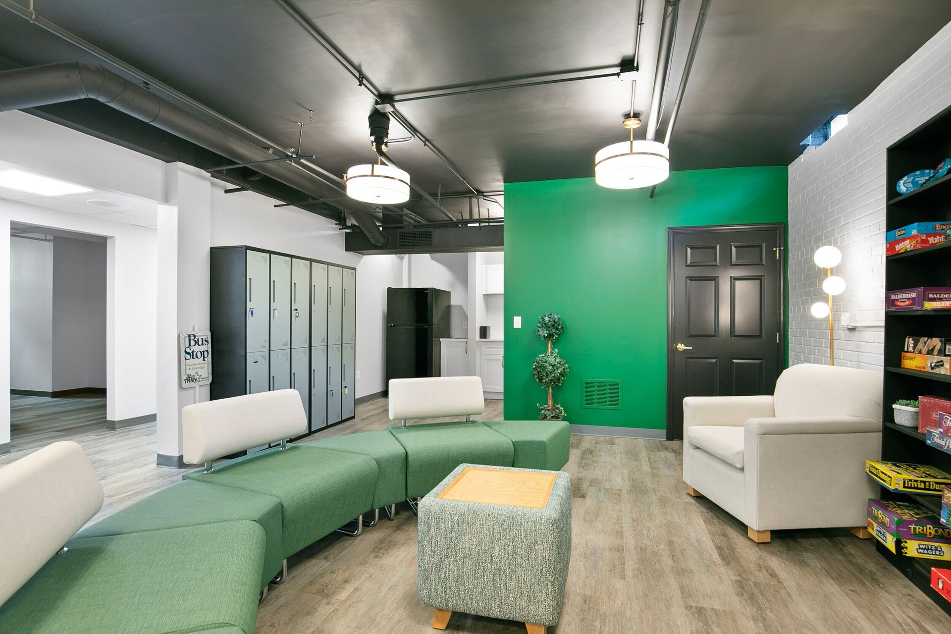 Modern living room with green accent wall, white chairs, sectional sofa, and wood flooring