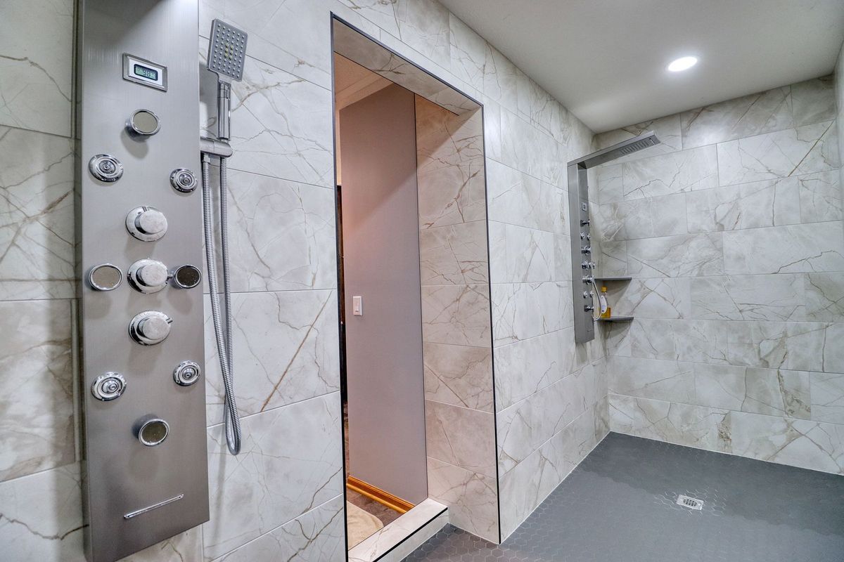 Modern shower with marble walls, glass door, and chrome control panel; built-in shelf on the right.