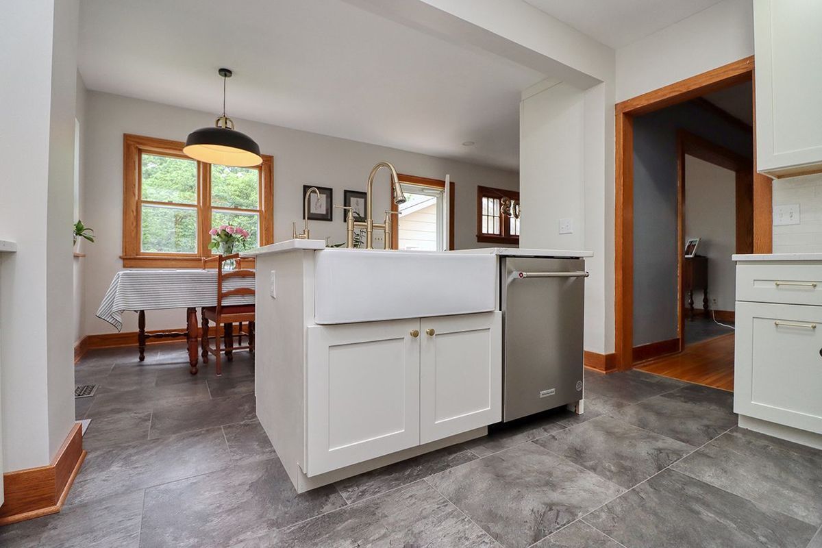 Modern kitchen and dining area with white cabinets, gray floors, and a wood table by a window.