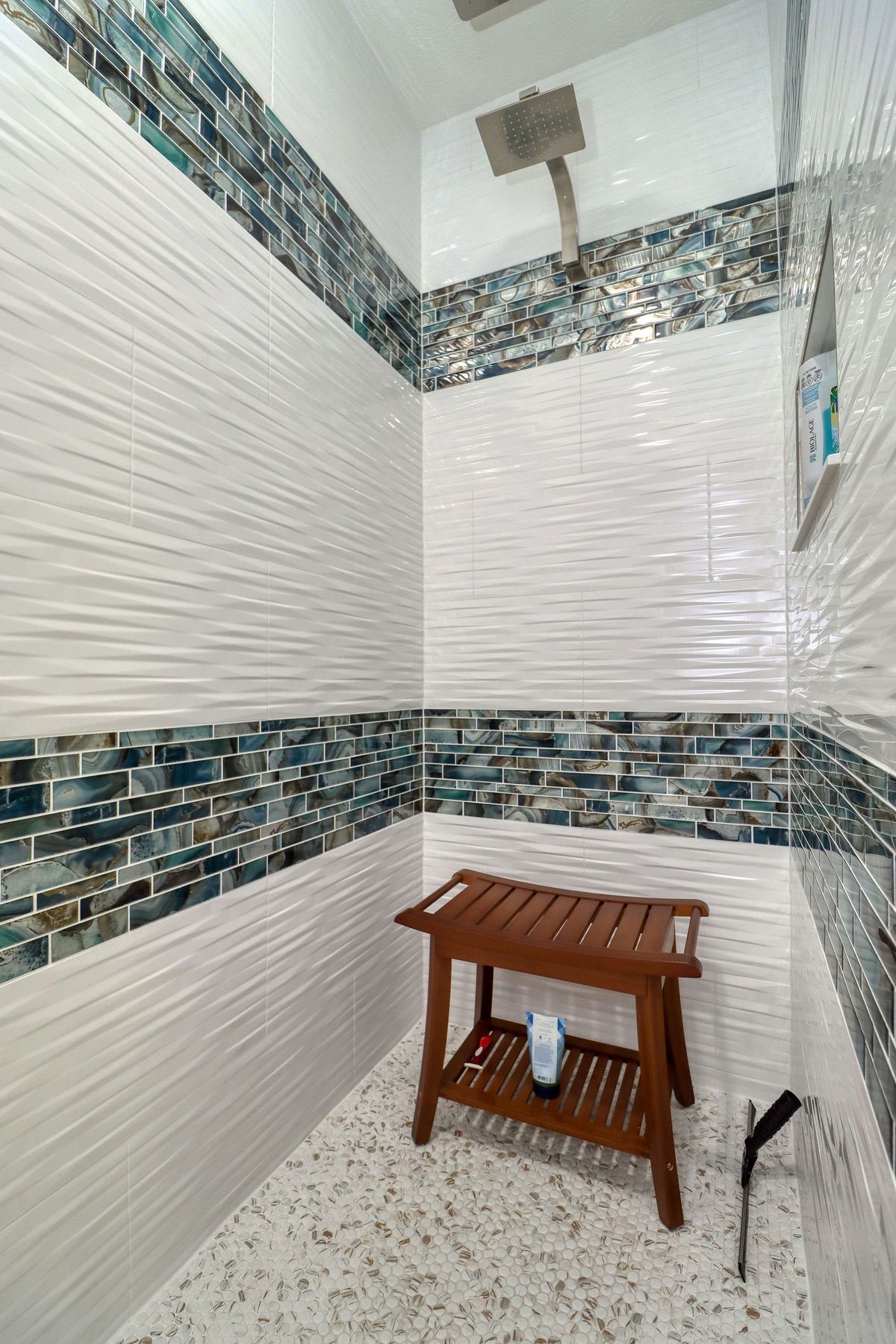 Small tiled shower stall with a wooden stool and handheld showerhead.