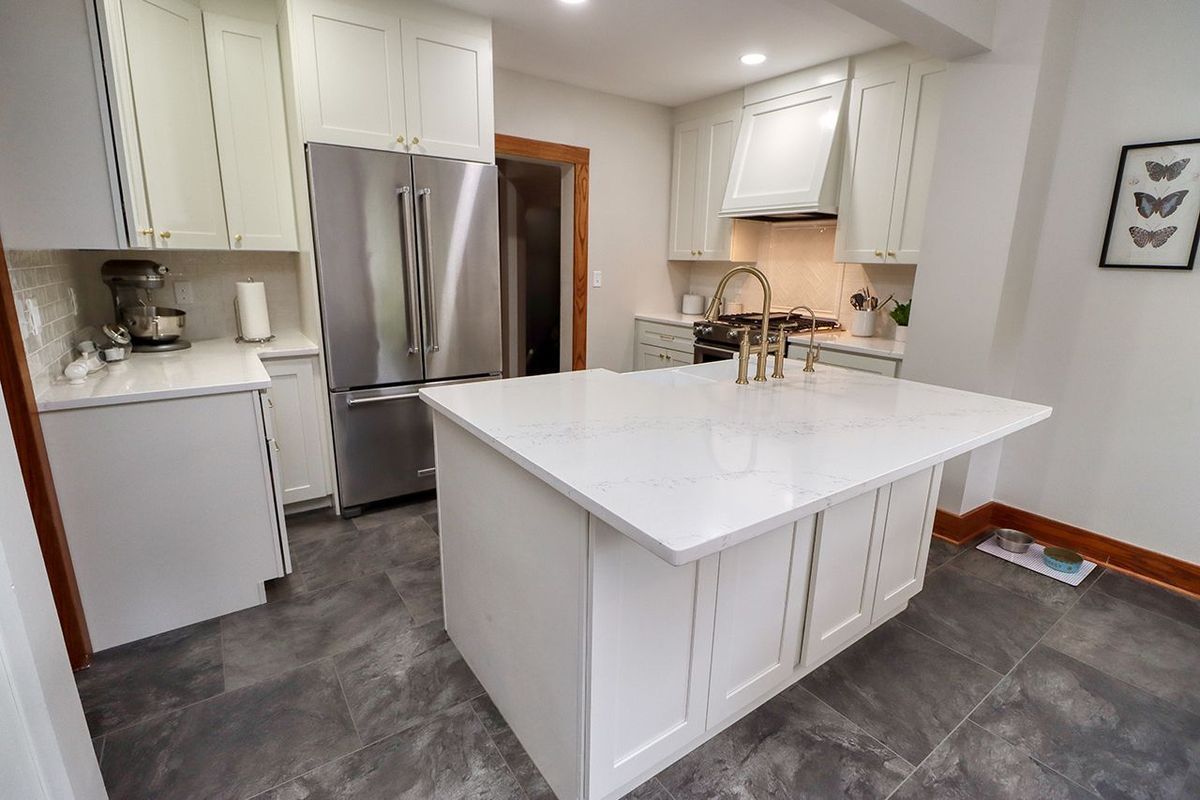 Bright white kitchen with stainless fridge, large island, gray tile floor, and small dining nook
