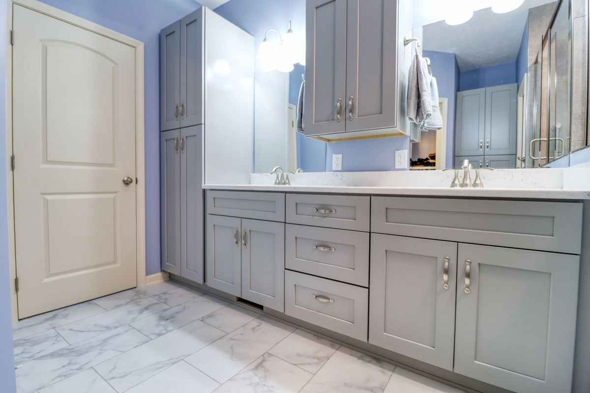 Elegant bathroom with gray cabinetry, large mirror, white countertop, and marble tile flooring.