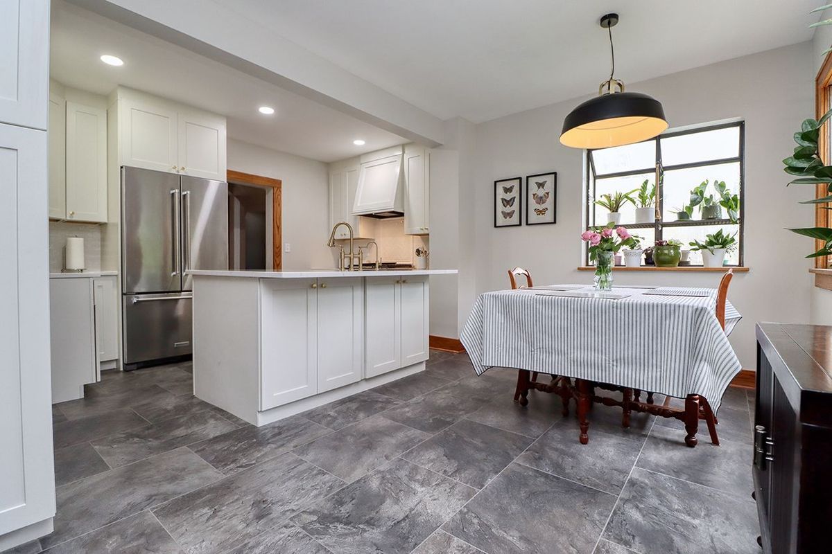 Bright modern kitchen and dining area with white island, gray floor, and table set by a window.