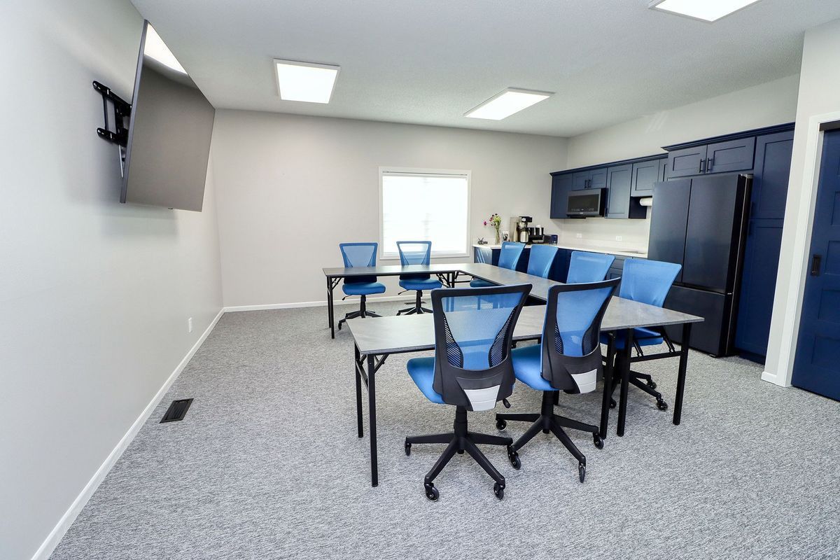 Modern conference room with blue chairs, white tables, wall-mounted TV, and lockers along the side.