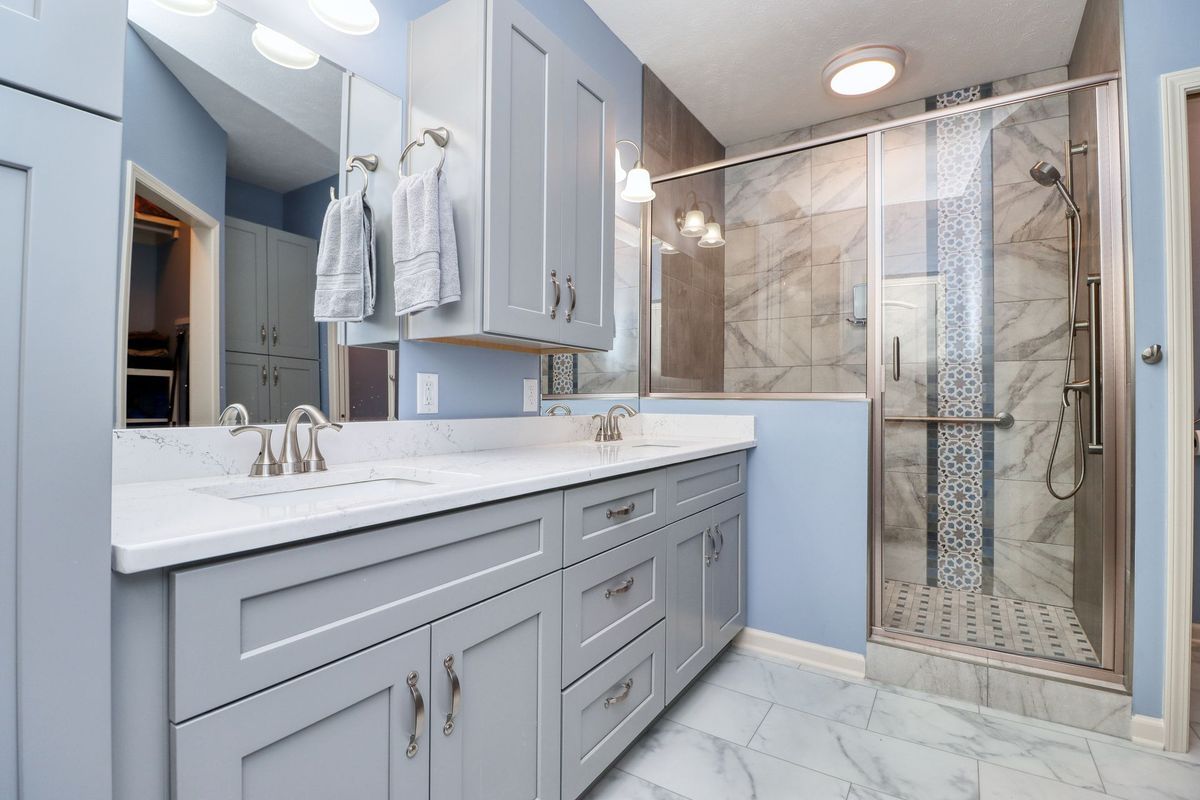 Bright modern bathroom with gray vanity, large mirror, and glass-enclosed shower.
