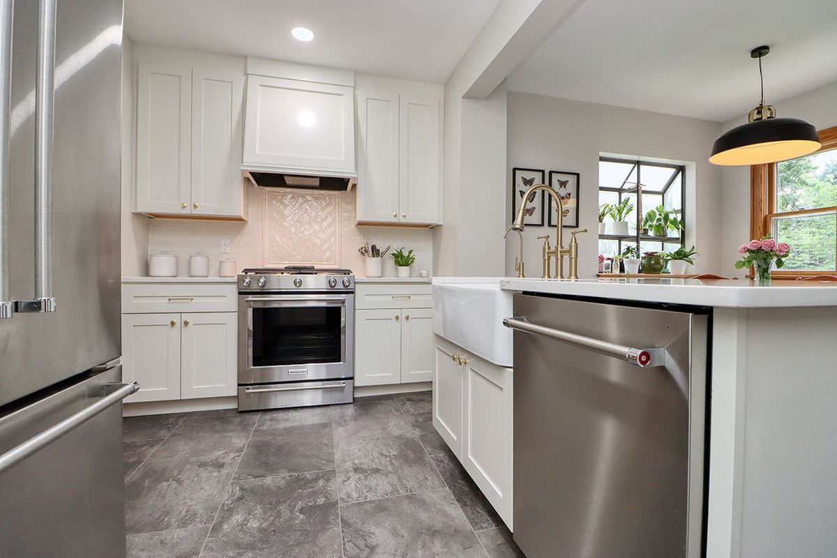 Bright white kitchen with stainless steel appliances, gray floor, and a windowed island.