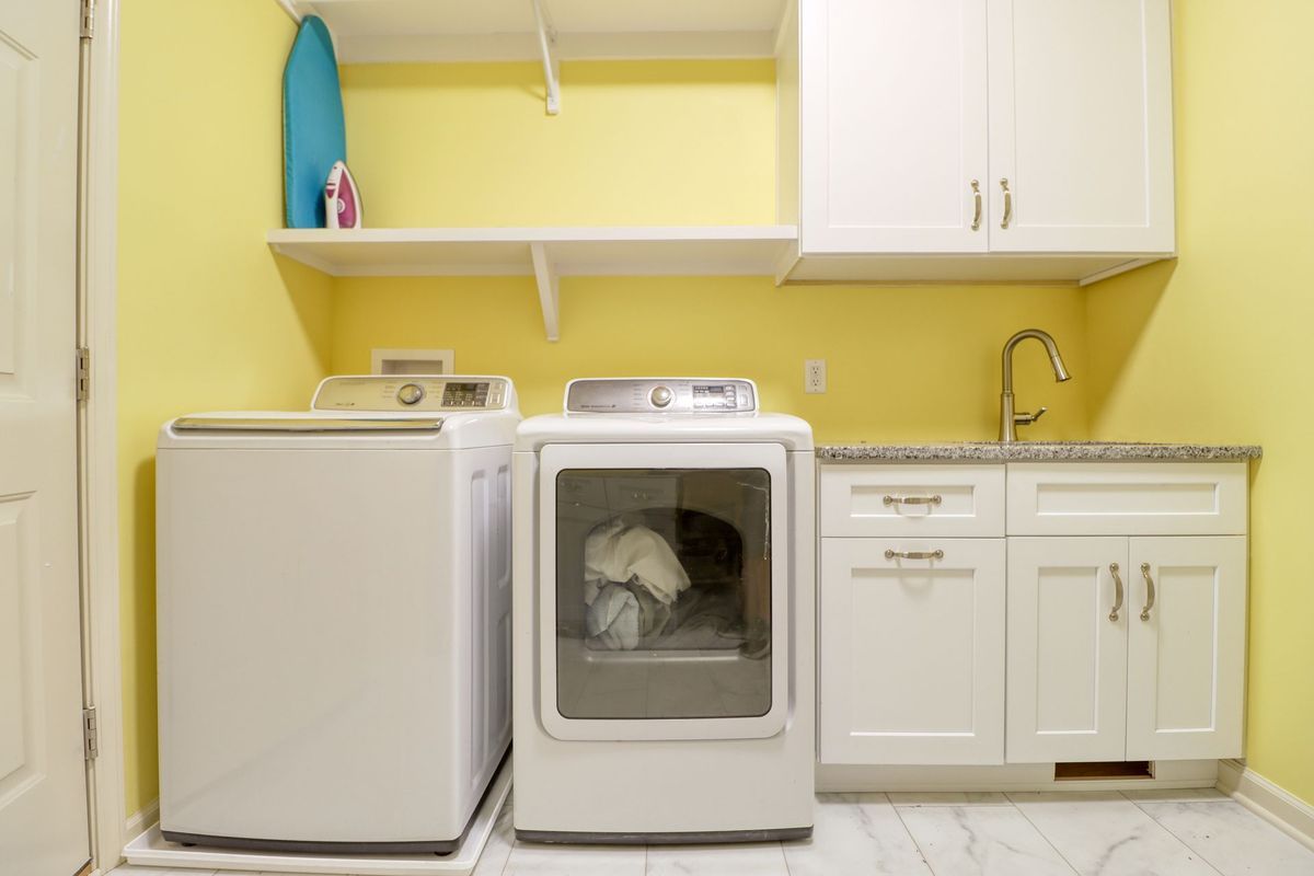 Yellow laundry room with white washer, dryer, cabinets, sink, and a small fridge.