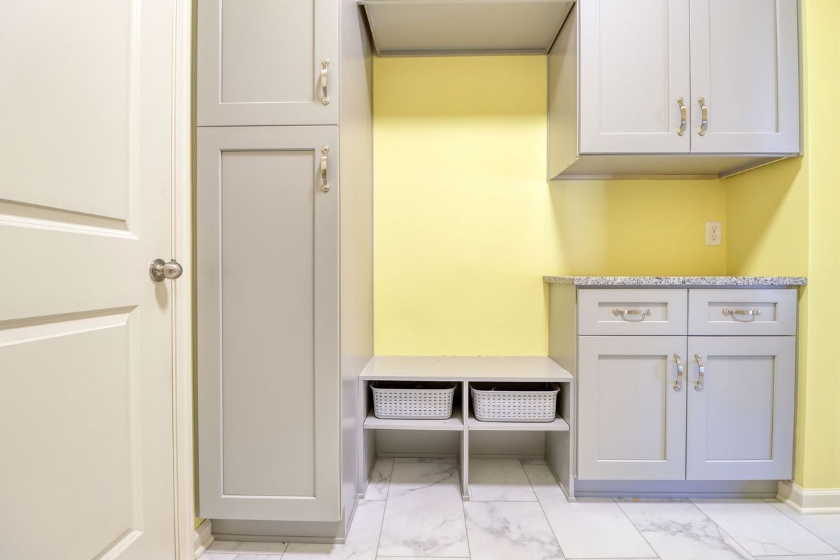 Built-in laundry nook with gray cabinets, yellow wall, countertop, and two storage baskets under a hanging rod