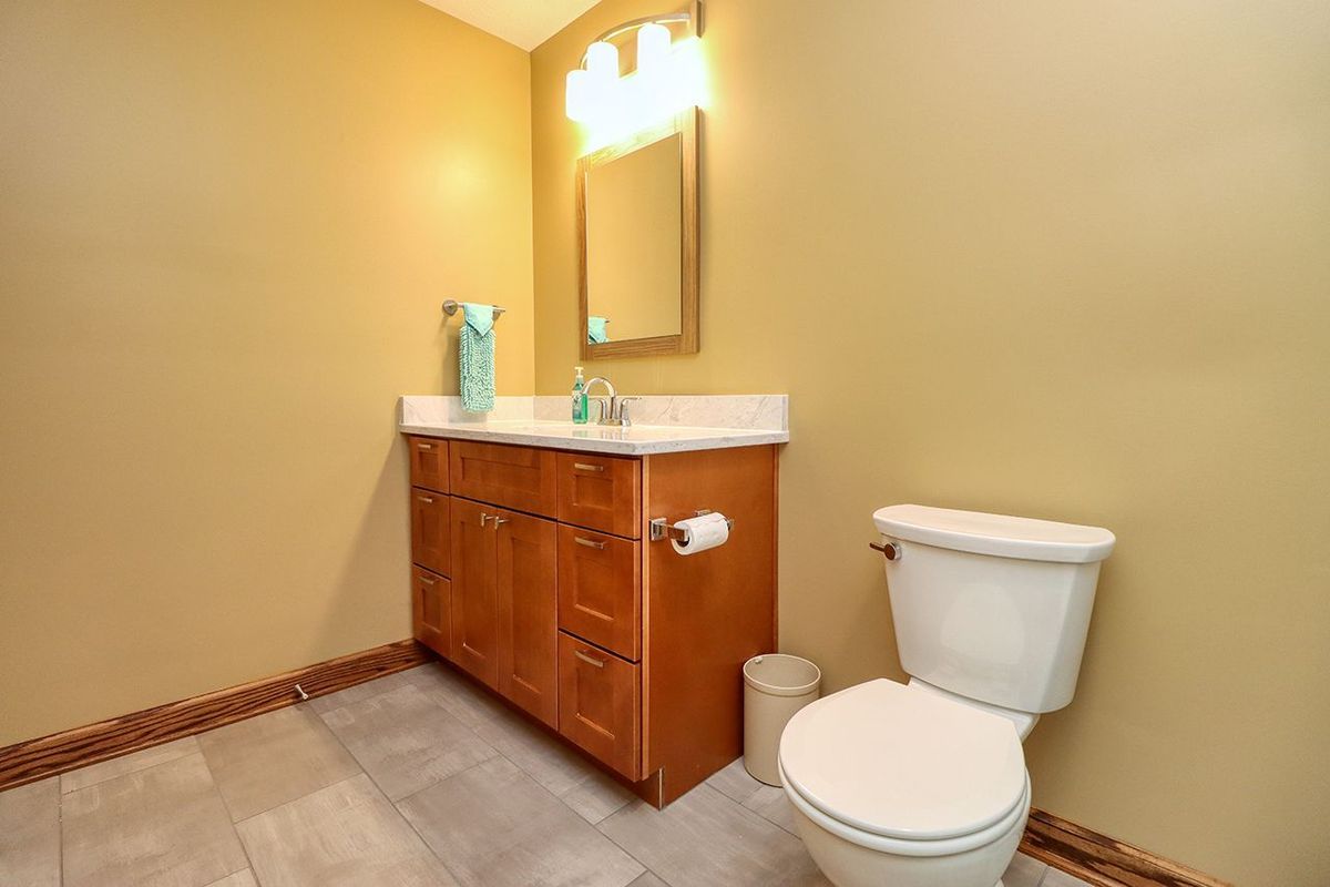 Small beige bathroom with wooden vanity, mirror, and white toilet.