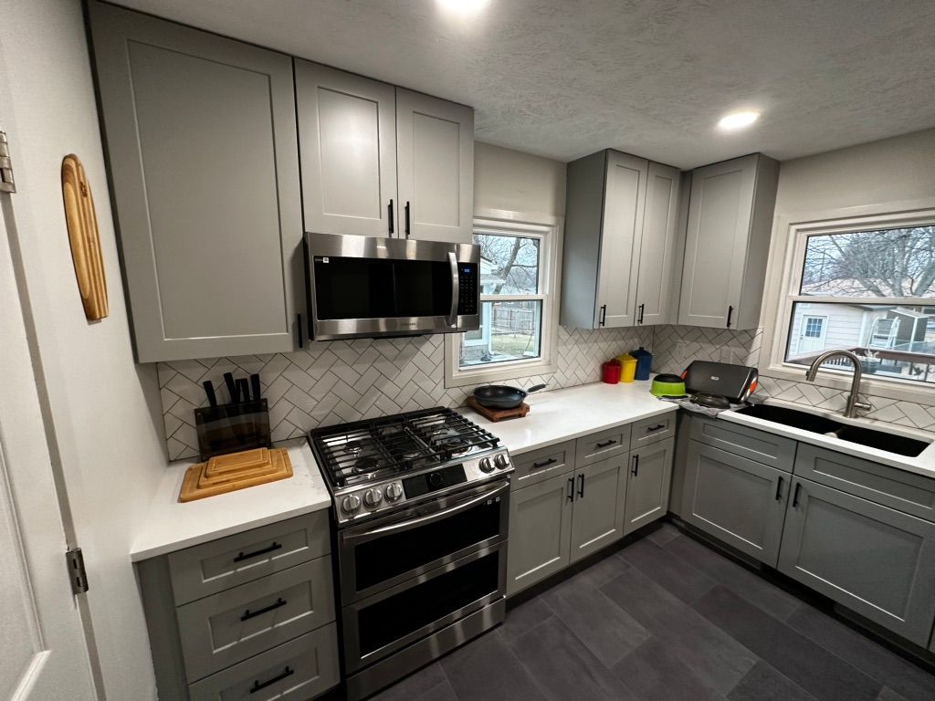 Modern gray kitchen with stove, cabinets, herringbone backsplash, and large windows