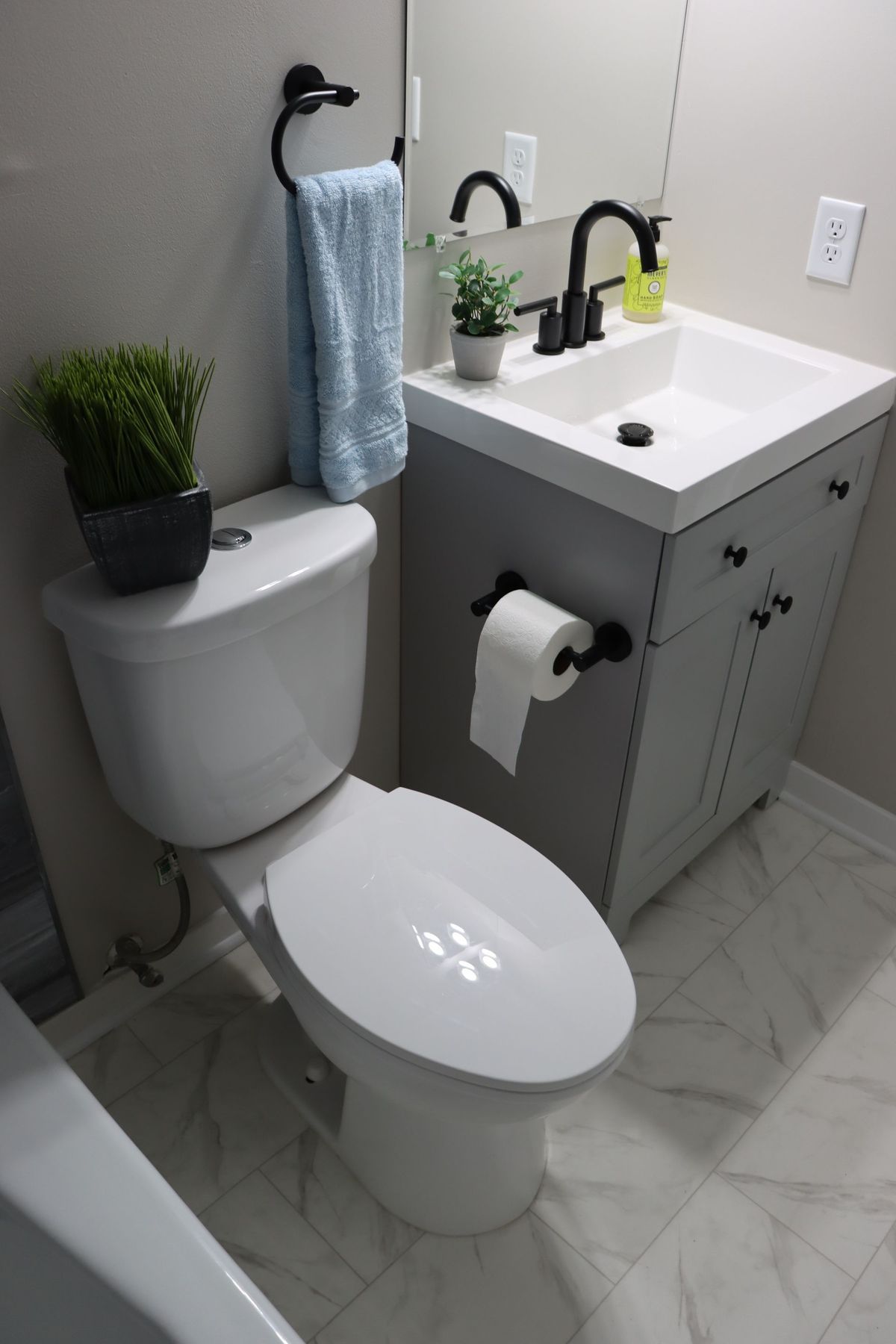 Small modern bathroom with white toilet, gray vanity, sink, black fixtures, and towel.