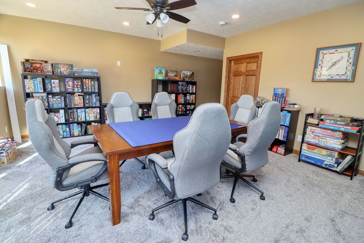 Bright game room with a table, six swivel chairs, and shelves of board games and books.