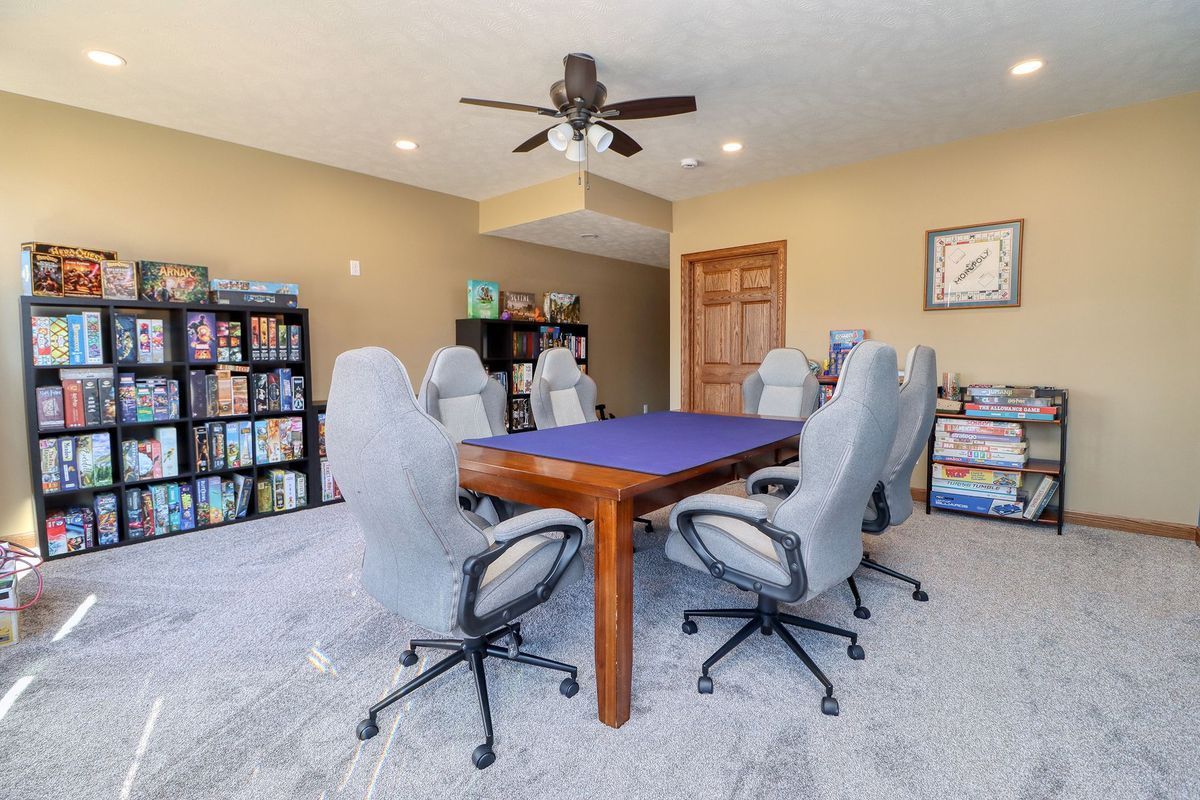 Game room with a wooden table, four swivel chairs, board games on shelves, and a ceiling fan.