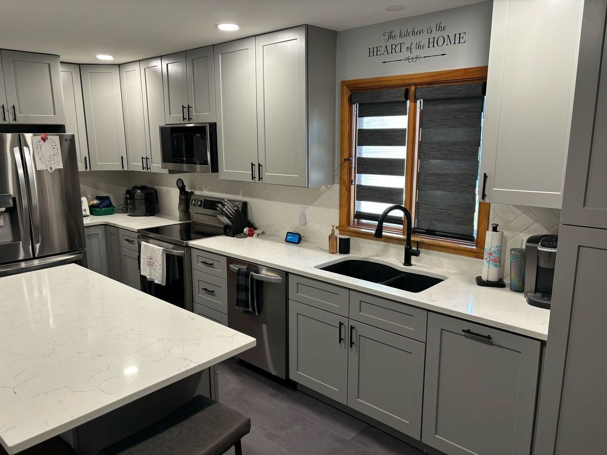 Modern kitchen with gray cabinets, white countertops, stainless appliances, and a window above the sink