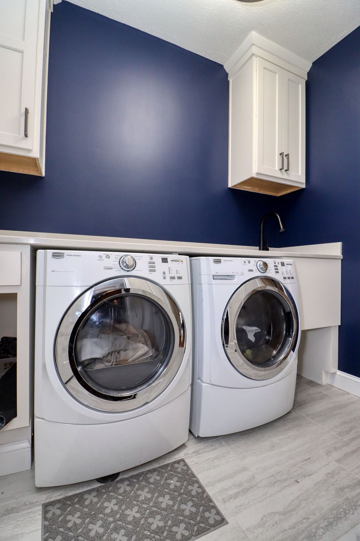 Laundry room with front-loading washer and dryer beneath blue walls and white cabinets