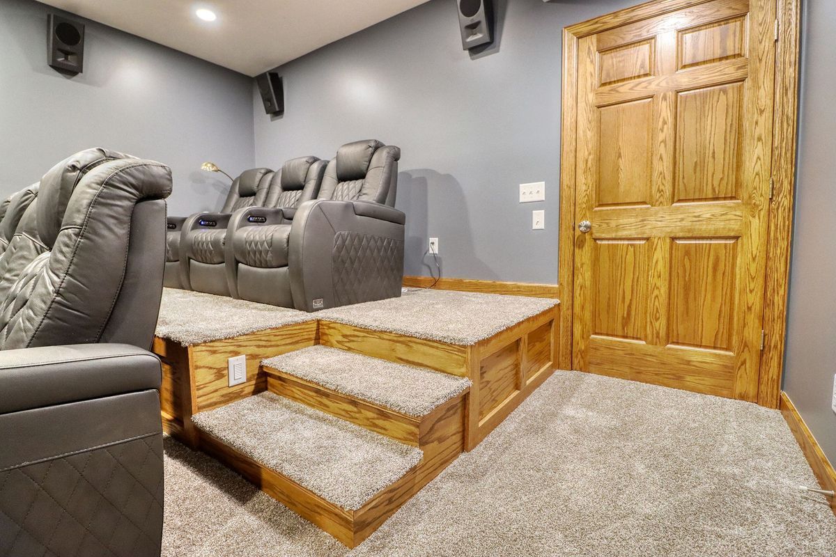 Home theater with gray reclining seats, carpeted steps, and wood double doors on the right
