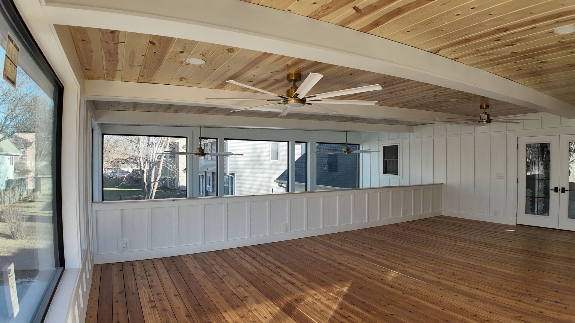 Empty room with wood floors, white paneled walls, exposed beams, and large windows.