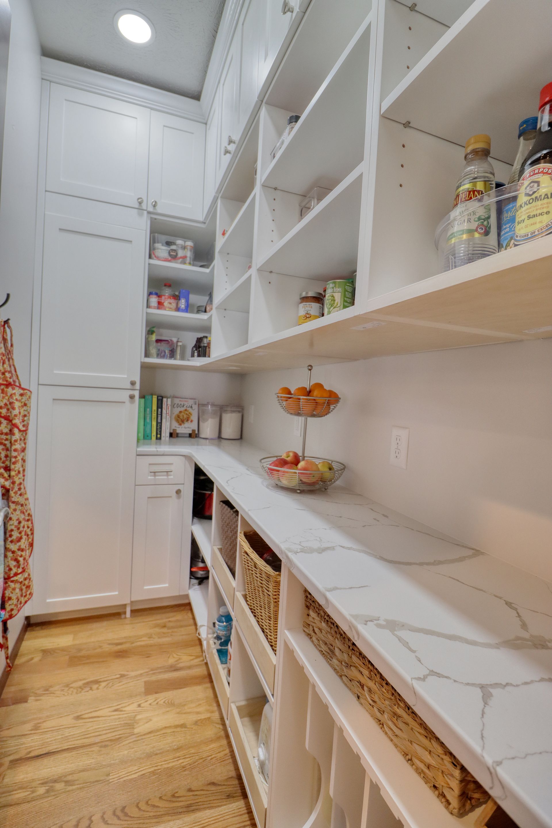 Bright white pantry closet with open shelves, woven baskets, and marble-look countertop in a narrow hallway.