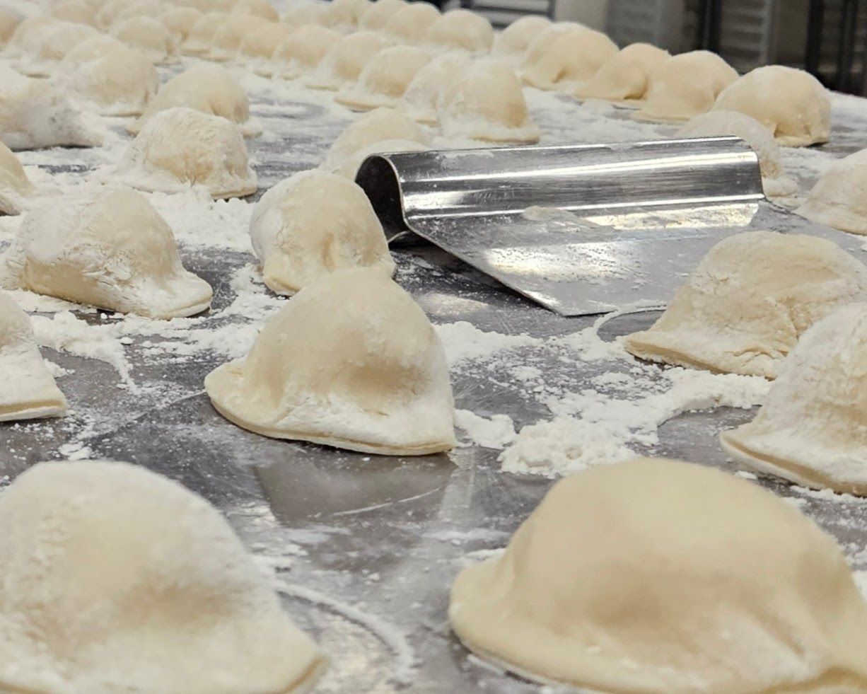 Fresh pasta dumplings on a floured surface with a metal dough cutter in the background