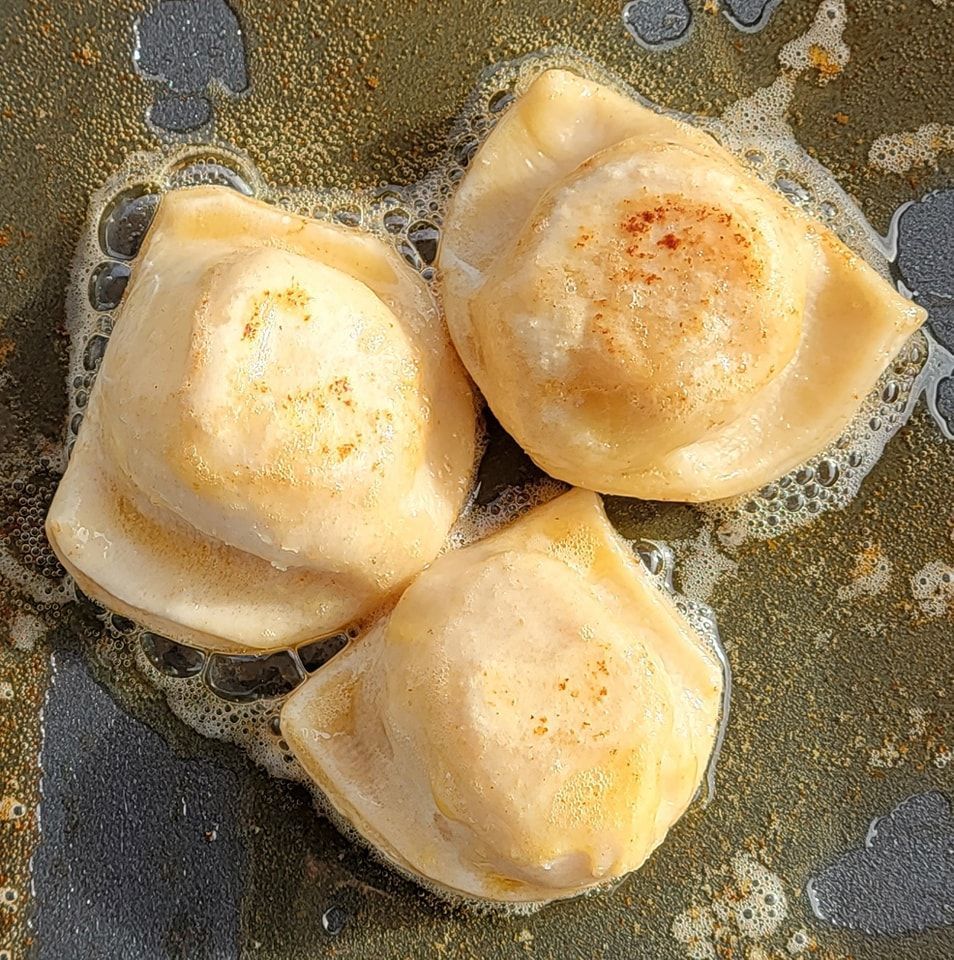 Three pierogi are being cooked in a frying pan