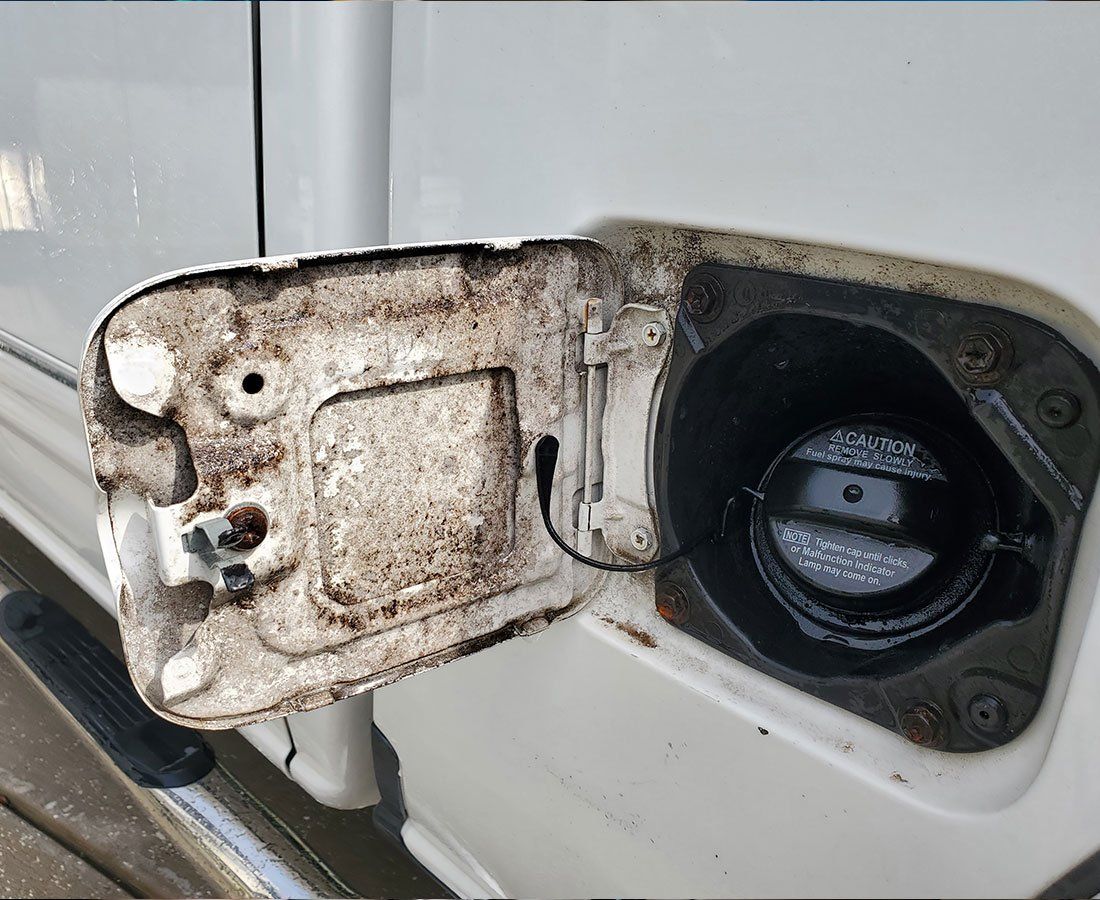 Opened white fuel door with black cap and dirty interior.