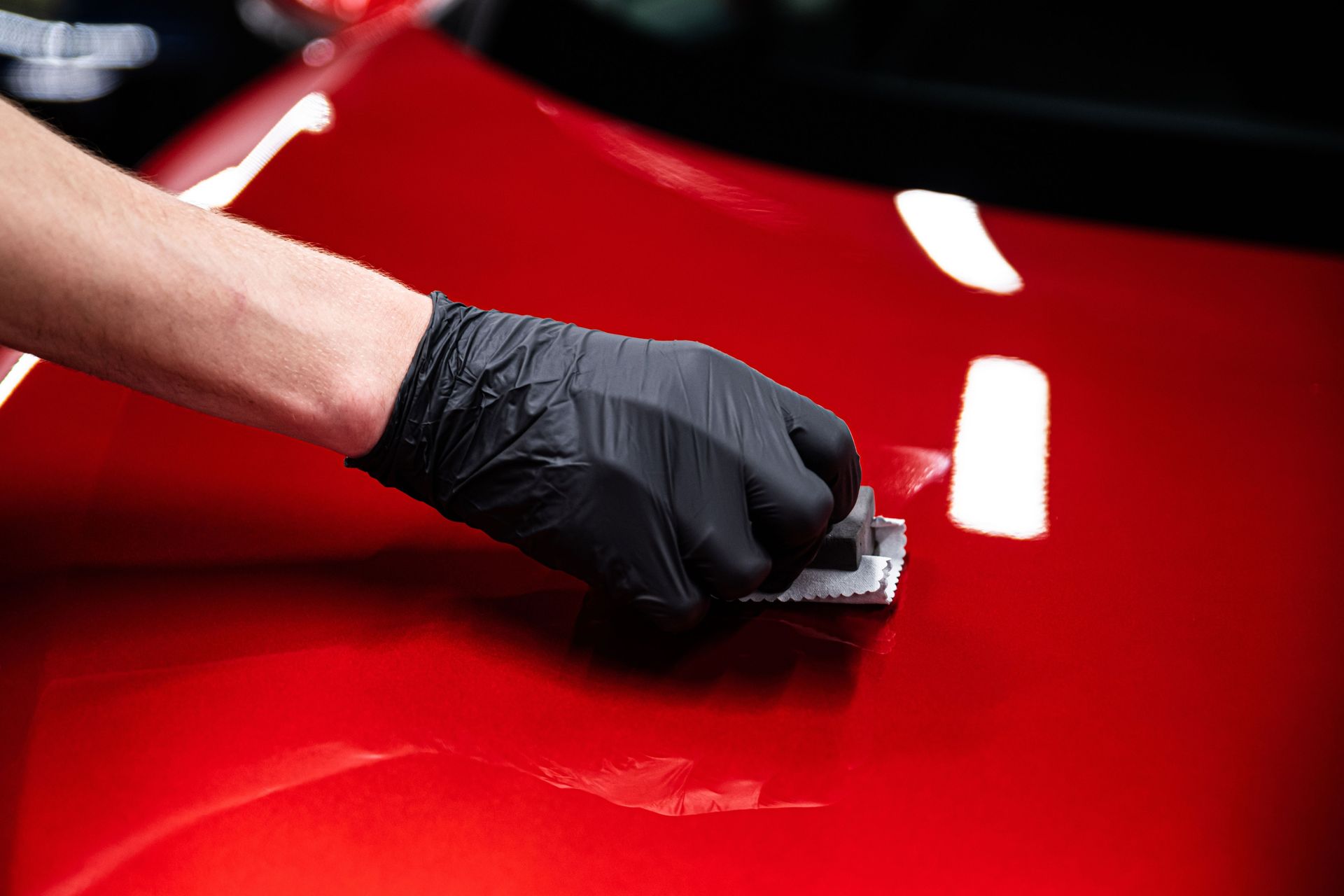 Person in black glove applies ceramic coating to red car surface.