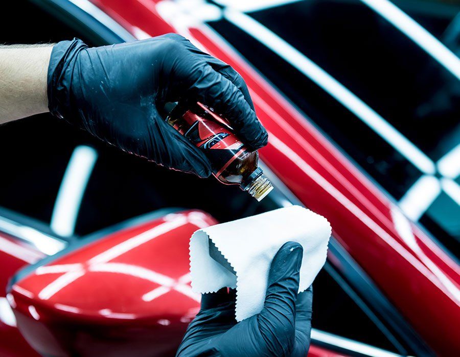 Hands in black gloves applying ceramic coating to a red car with a white cloth.