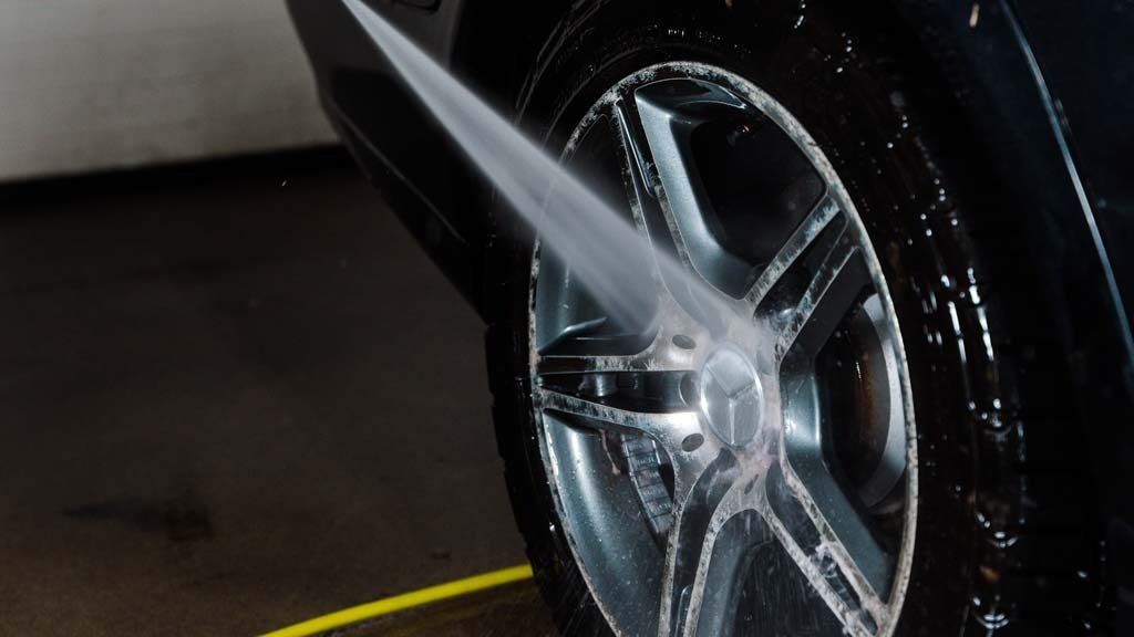 Washing a car wheel with a high-pressure water spray, chrome rim, black tire, and car body.