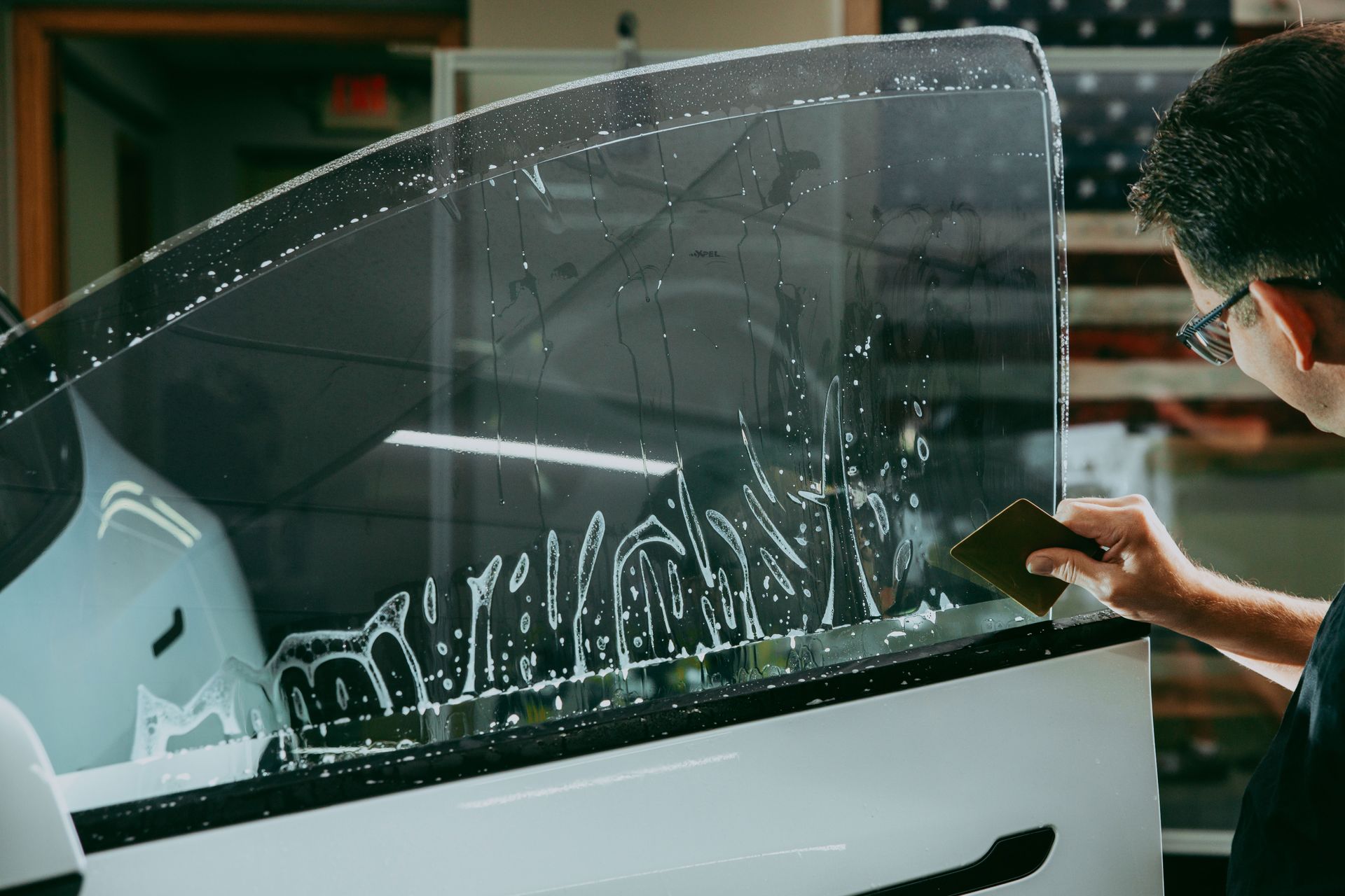 Person applying window tint to a car window with a squeegee.