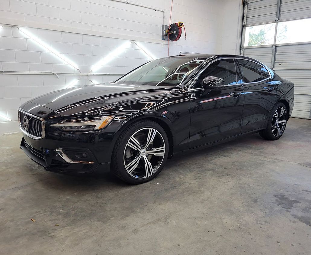Black Volvo sedan in a garage, shiny paint, front view, bright lights above.