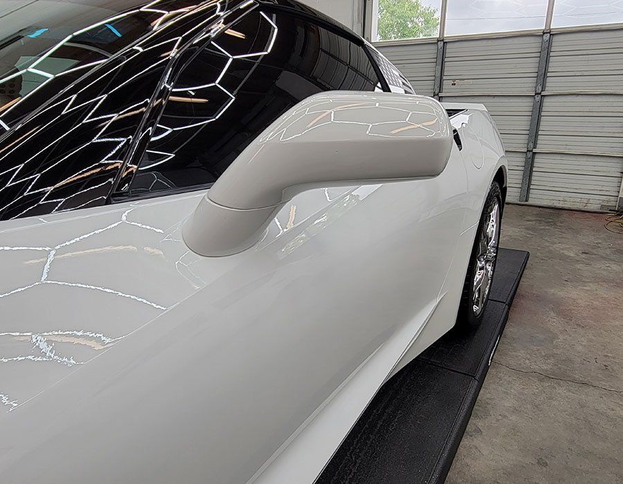 White sports car, side view, showing side mirror and shiny paint in a garage setting.
