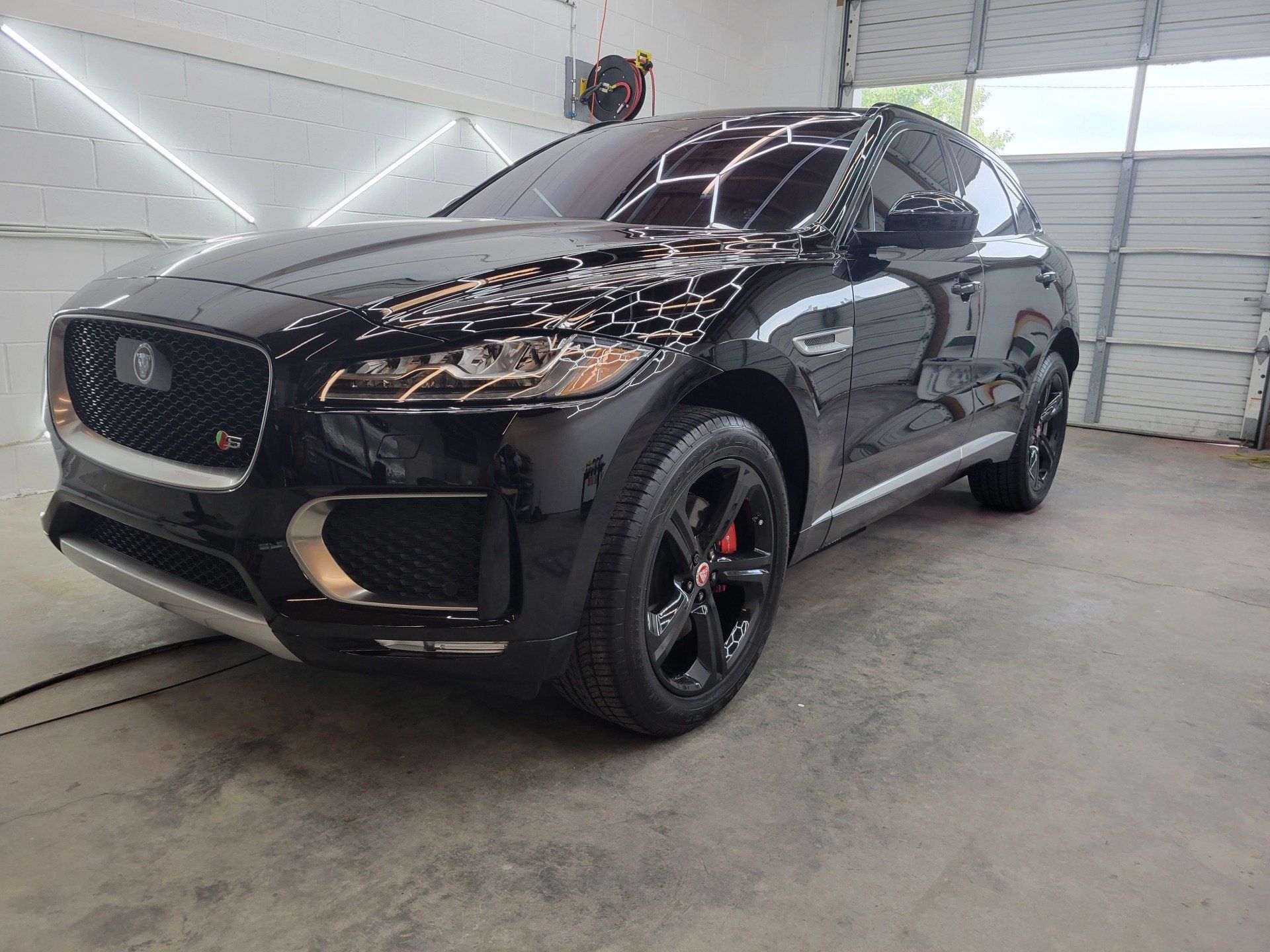 Black Jaguar F-Pace SUV parked in a garage. Shiny exterior, black wheels, red brake calipers.