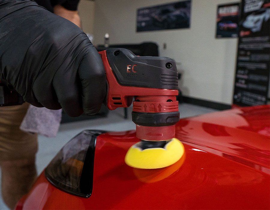 A person polishes a red car using a red and black electric buffer.