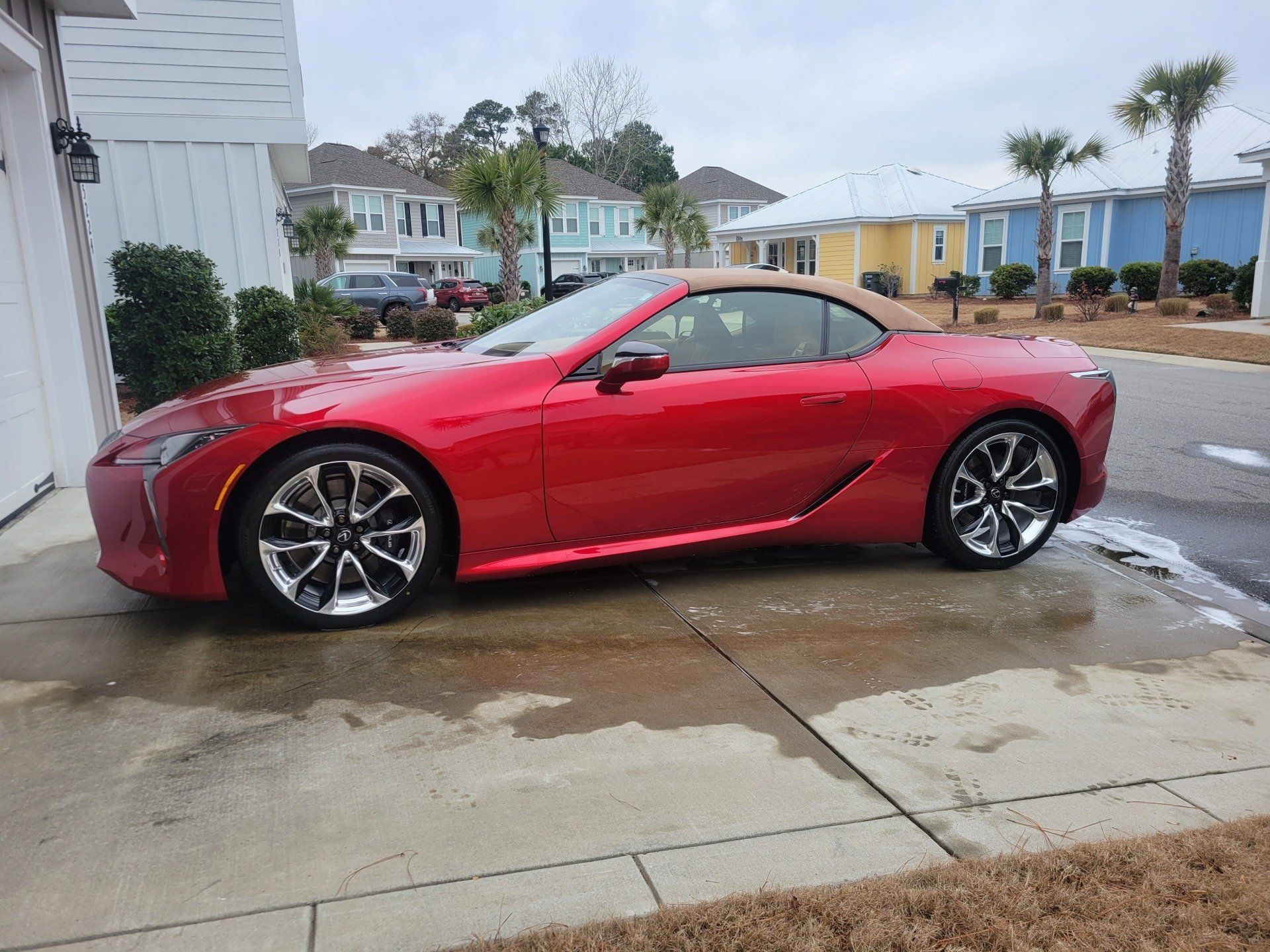 Red convertible car parked in front of a white garage, next to a sidewalk in a residential neighborhood.