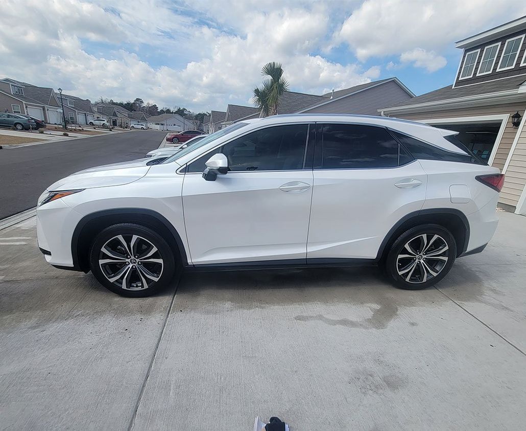White Lexus SUV parked on a concrete driveway, next to a house with a gray roof.