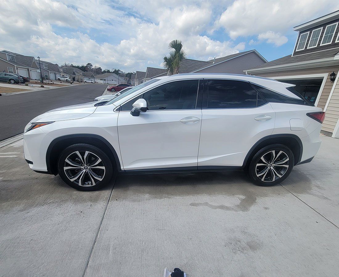 White Lexus SUV parked on a concrete driveway, next to a house with a gray roof.