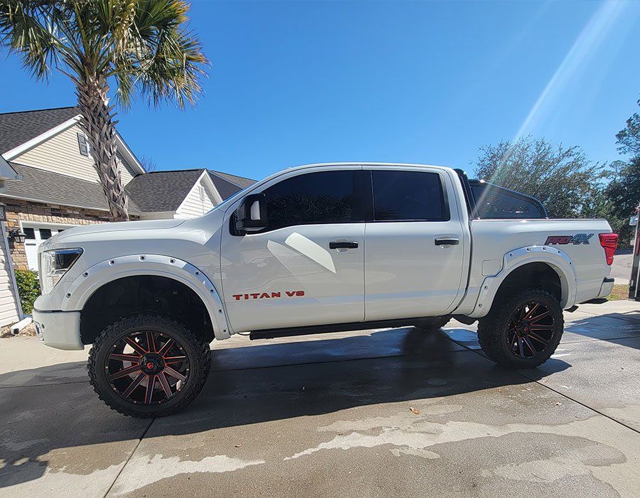 White Nissan Titan truck with lifted suspension and custom wheels parked outside.