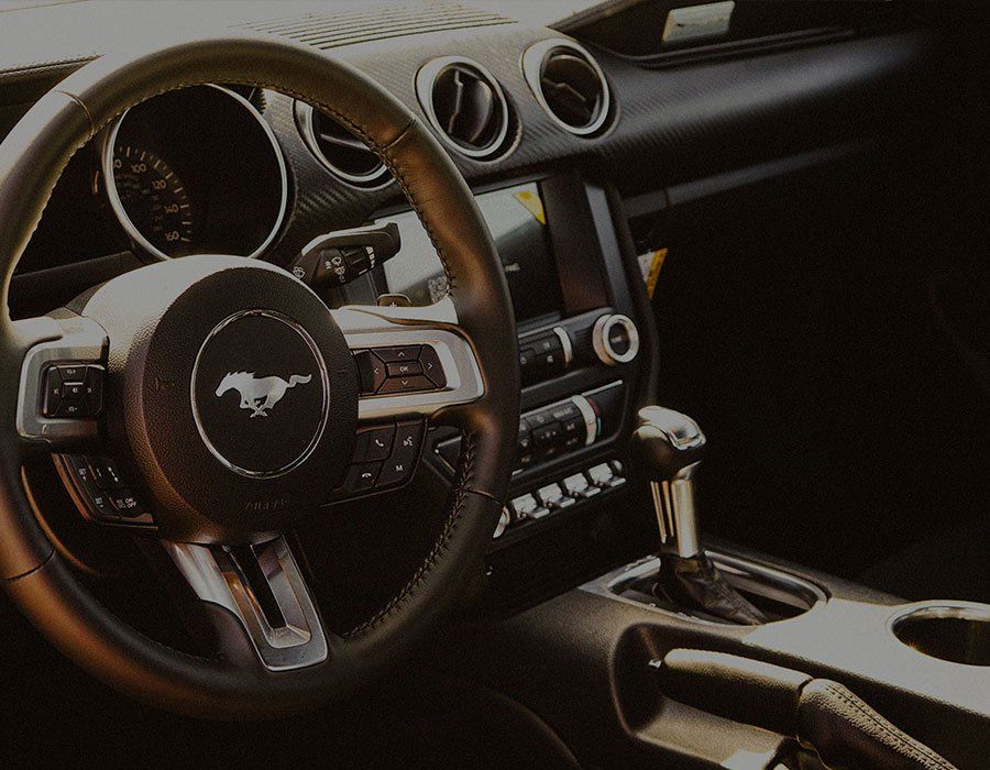 Interior of a Ford Mustang, showing the steering wheel with the Mustang logo, dashboard, and gear shift.
