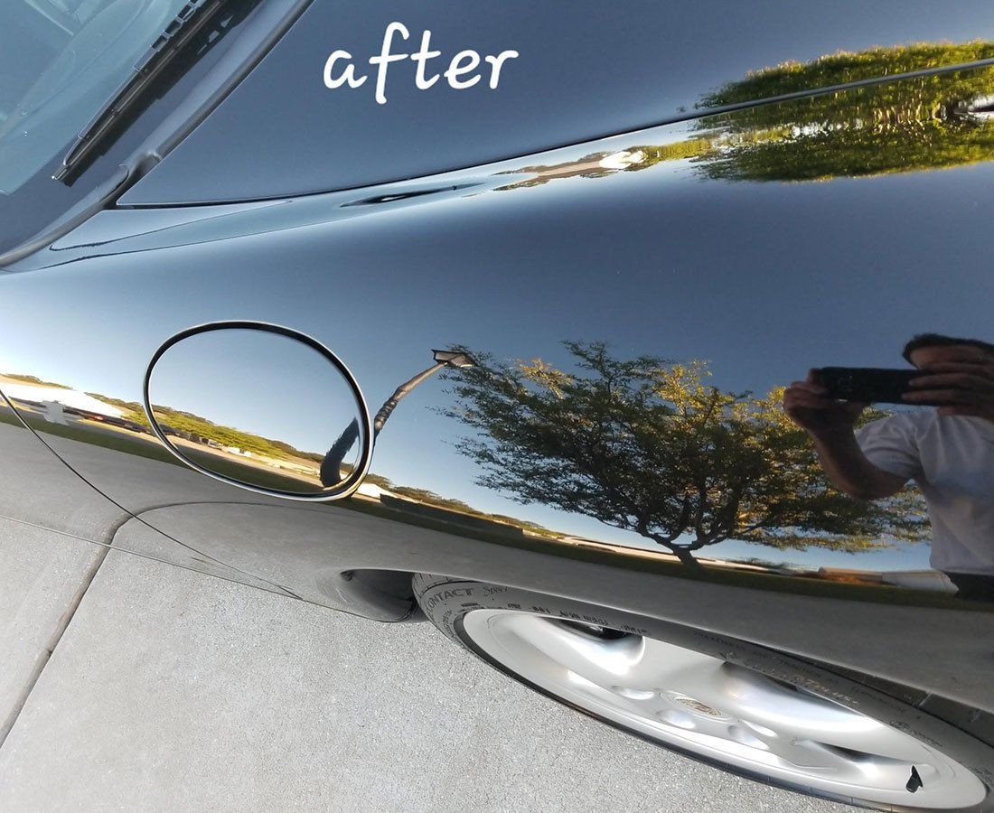 Close-up of a black car's shiny surface, reflecting a tree and sky; the fuel door is visible.