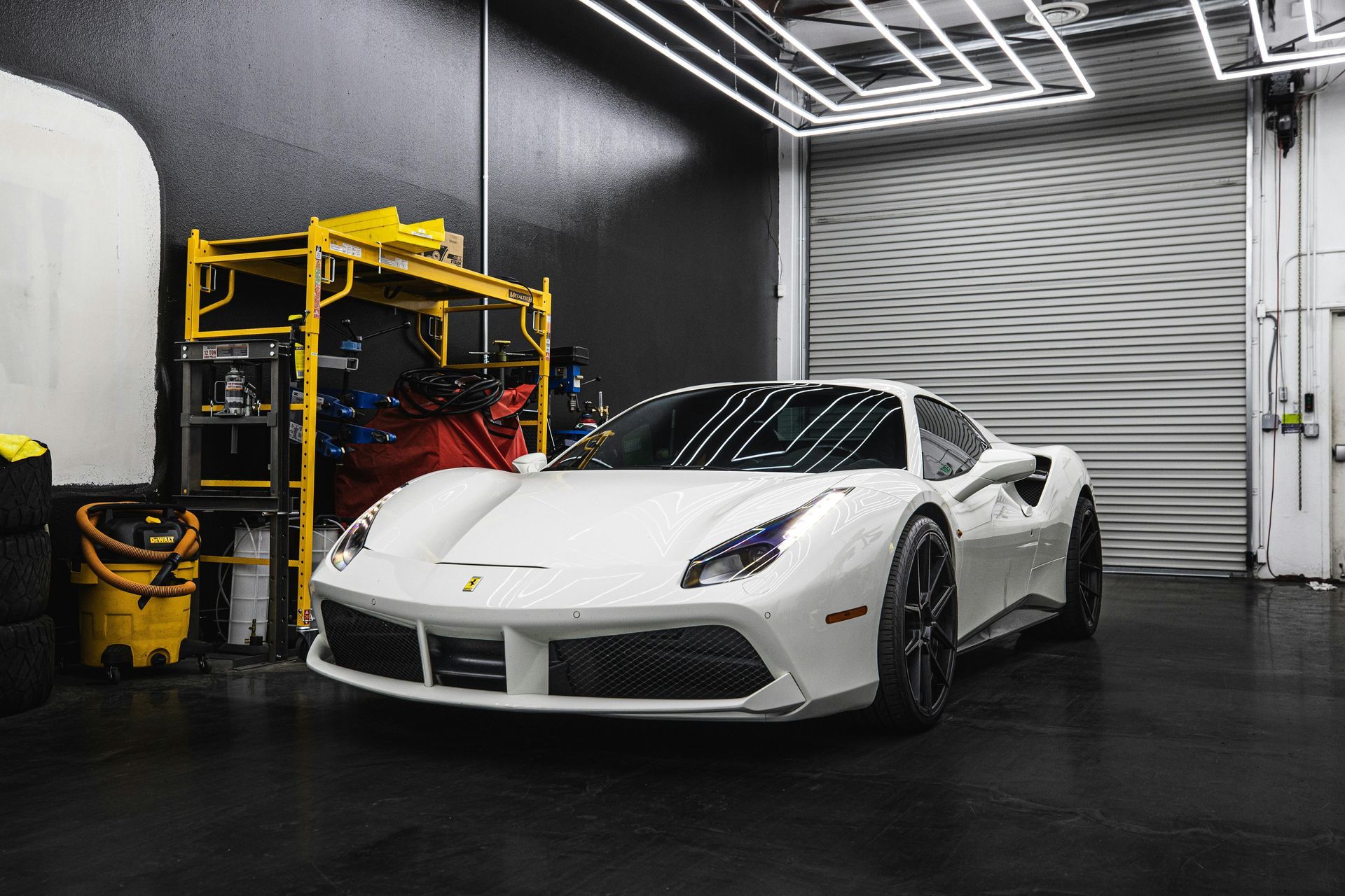 White Ferrari sports car inside a garage, with work lights and equipment visible.